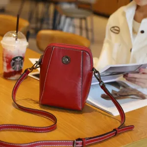 Detail view of red leather crossbody phone bag on cafe table, featuring metal floral accent.