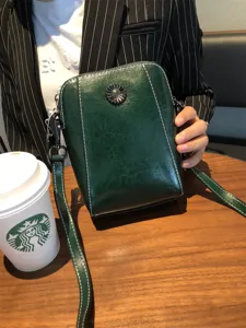 Detail view of a retro dark green leather crossbody phone bag with floral metal snap.