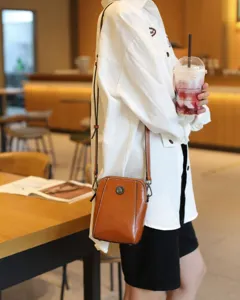 Vue détaillée du sac bandoulière en cuir ciré marron, fond style de vie de café décontracté.