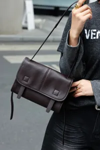 Close-up detail of the brown leather messenger bag showing premium texture and dual strap design.