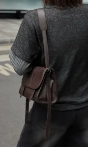 Close-up of a brown leather messenger bag worn crossbody, showcasing daily commuting style.