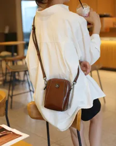 Vue lifestyle détaillée d'un sac bandoulière marron en cuir ciré porté dans un café.