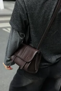 Detail view of dark brown leather crossbody messenger bag, retro style, high texture.