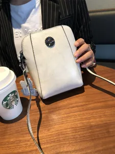 Detail shot of white leather crossbody phone bag with floral metal clasp and strap.