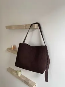 Detail view of a large capacity brown suede shoulder bag hanging on a minimalist stone shelf.