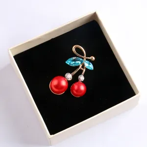 Detailansicht einer Kirschen Brosche mit blauen Kristallen und roten Perlen im Schmuckkästchen.