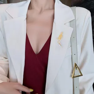 Elegant gold wheat ear brooch with pearl accent worn on white blazer for women fashion style.