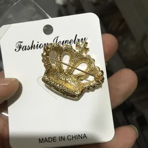 Goldfarbene Kreuz-Kronen-Brosche mit Trägerkarte, elegantes Modeaccessoire für Alltag.