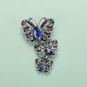 Détail de broche papillon triple en alliage argenté vintage avec des strass bleu foncé.