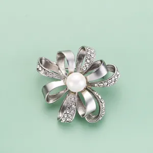 Vue détaillée d'une broche fleurie argentée avec strass en cristal et perle centrale.