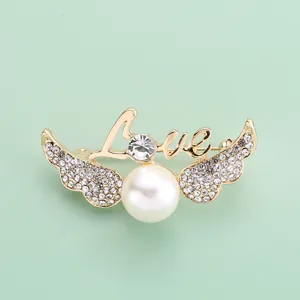 Gros plan détaillé de la broche ailes d'ange dorée avec des strass étincelants et une grande perle.