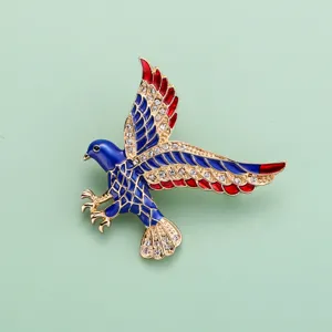 Gros plan broche aigle avec émail bleu rouge, bordure dorée et strass scintillants.