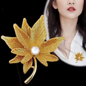 Dettaglio spilla perla foglia d'acero dorata, elegante accessorio pianta per abiti donna.