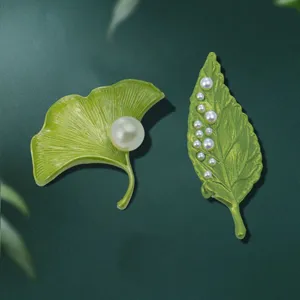 Primo piano sui dettagli della spilla con perle a foglia verde, accessorio elegante.