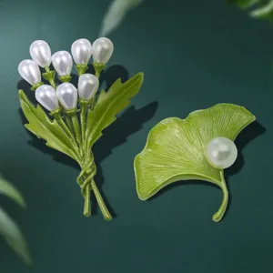 Primo piano ravvicinato del delicato set di spille con bouquet di perles e foglia di ginkgo.