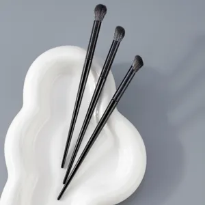 Detail shot of three professional black eye makeup brushes arranged neatly on a white ceramic tray.