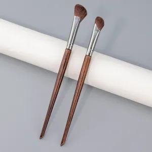 Gros plan détail de deux pinceaux de maquillage en bois avec poils bruns sur support.
