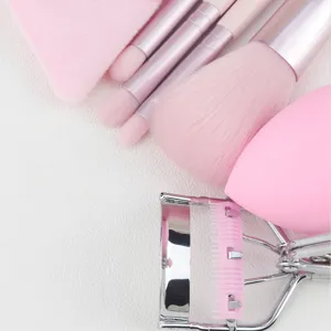 Detail shot of pink makeup brush set, eyelash curler and soft sponge puff for daily flawless makeup.