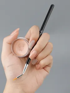 Angled detail makeup brush and concealer jar close-up view showing fine brush tip and pot.