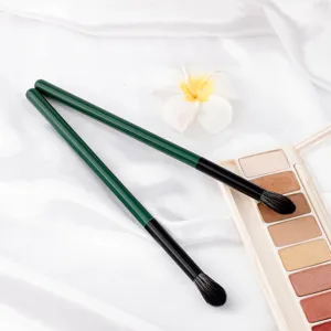 Detail shot of soft green handle makeup brushes on silky fabric with palette and white flower.