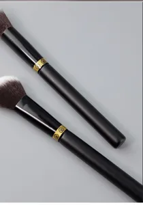 Makeup brush detail shot, black handle with gold ring, soft bristles for smooth blending.