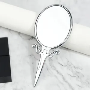 Detailansicht eines silbernen Vintage Klapphandspiegels mit verziertem Griff und klarem Glas.