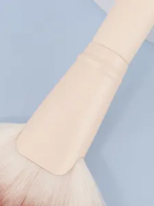 Close-up detail of large fan makeup brush with soft white bristles and nude handle.