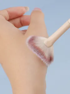Close-up detail of soft fan makeup brush testing on hand skin for smooth application and glow.