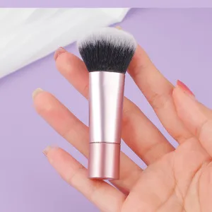 Close-up of a portable short-handled makeup brush with pink metal handle and soft bristles.