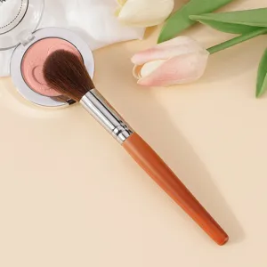 Detail view of a soft synthetic makeup brush with wooden handle and blush compact.