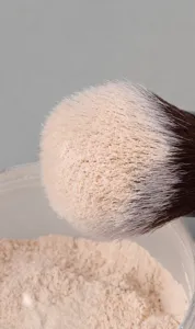 Detailed close-up shot of soft makeup brush bristles dipping into loose powder texture.