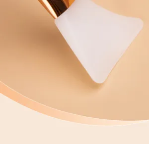 Détail de pinceau masque facial en silicone, tête blanche douce et poignée dorée.