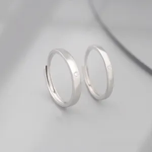 Gros plan detail anneaux de couple argent minimalistes avec petit diamant, design elegant.