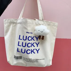 Detail view of canvas tote bag with lucky print and cute fluffy cloud charm pendant.