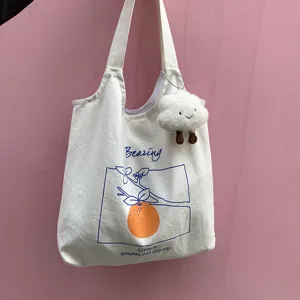 Close-up of white canvas tote bag with cute cloud plush pendant and blue orange print detail.