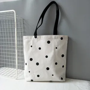 Dettaglio borsa shopper in tela, motivo a pois neri minimalista, tracolla lunga.