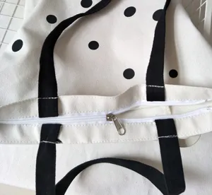 Dettaglio borsa shopper in tela, pois neri, chiusura con zip bianca, stile minimalista.