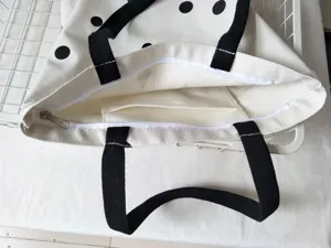 Dettaglio della borsa in tela con fantasia a pois, manici neri e pratica tasca con zip.