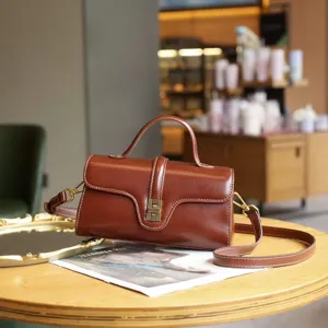 Vintage brown leather crossbody bag with top handle, elegant design and stylish metallic clasp.