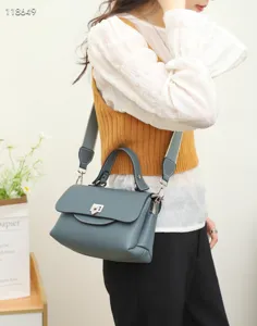 Detailed view of grey-blue leather handbag showing texture, metal lock, and wide strap.
