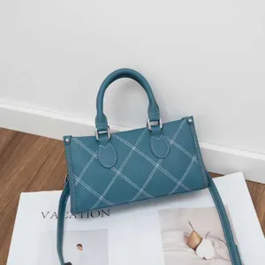 Close-up view of a stylish teal leather shoulder bag with contrast white stitching details.