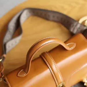 Close-up detail shot of vintage brown genuine leather cylinder bag with fine stitching.