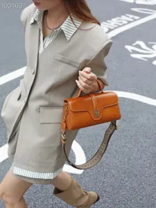 Stylish vintage leather shoulder bag detail, brown cylinder design with wide woven strap.