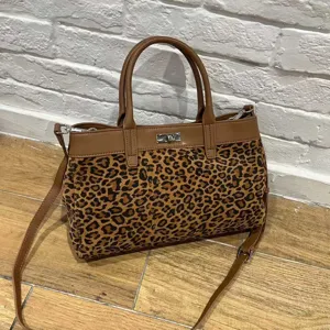 Close-up detail of stylish brown leather and leopard print handbag with metal turn-lock.