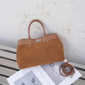Detailed view of brown suede colorblock tote bag with top handle and metal turn lock closure.