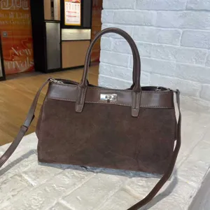 Detailed close-up view of elegant brown suede top-handle tote bag with metal turn-lock and strap.