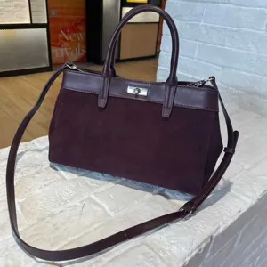 Burgundy suede handbag detail, metal turn-lock closure, structured top handles and strap.