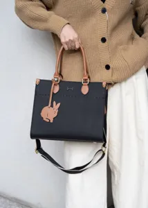 Vista dettagliata della borsa tote in pelle nera con manici marroni e ciondolo.