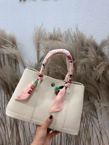 Dettaglio ravvicinato di borsa in vera pelle color crema con manico in foulard.