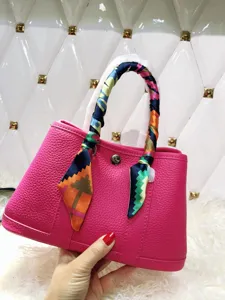 Dettaglio borsa rosa mostra consistenza della pelle e sciarpa colorata avvolta sul manico.